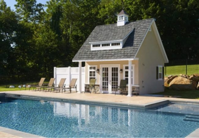 Modern prefab pool house beside a luxury backyard swimming pool with outdoor lounge furniture and landscaped garden.