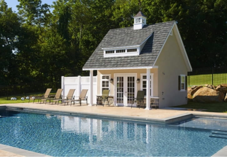 Modern prefab pool house beside a luxury backyard swimming pool with outdoor lounge furniture and landscaped garden.